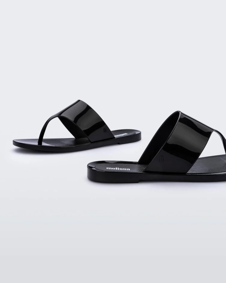 Side view of a pair of black Melissa Essential Chic Flip Flops with a wide upper strap.
