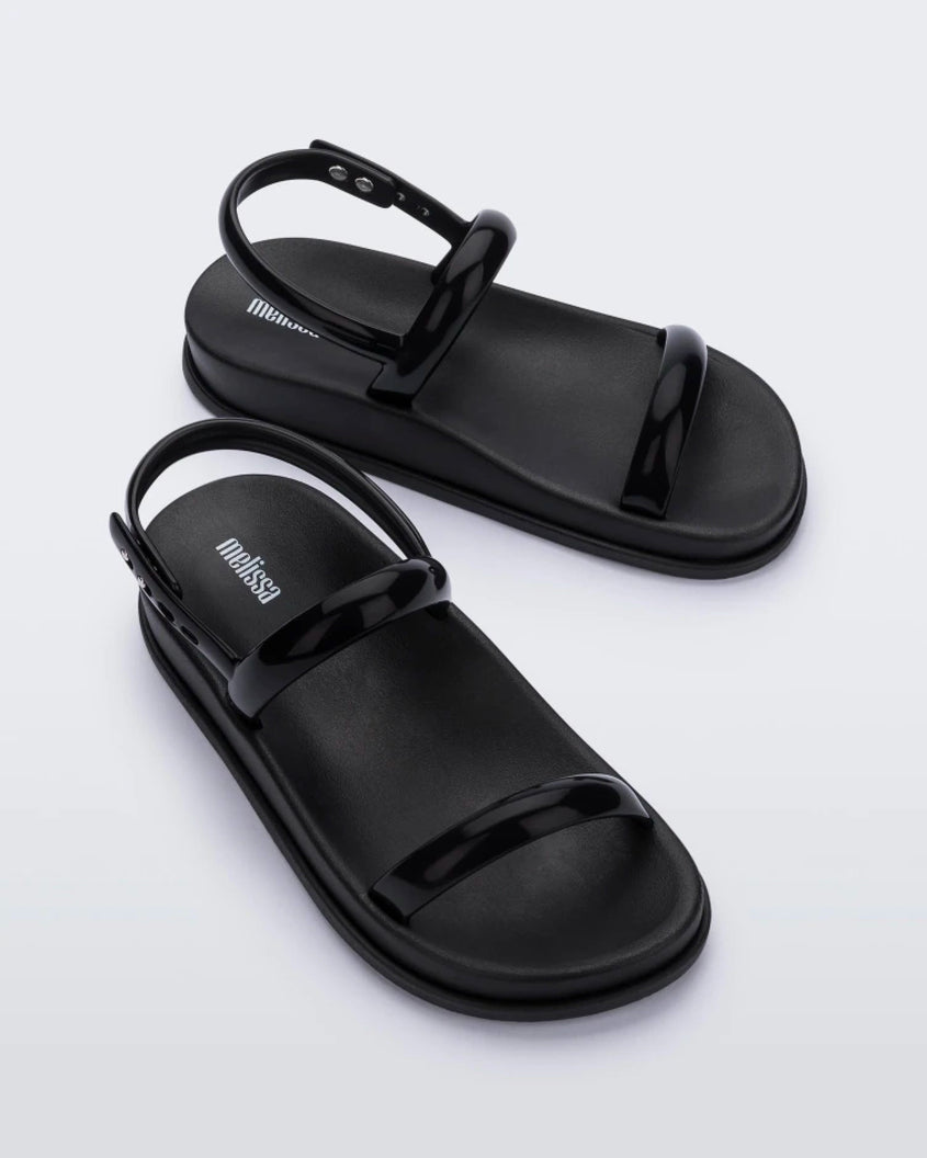 An angled top view of a pair of black Melissa Soft Wave Sandals with a front and ankle strap.
