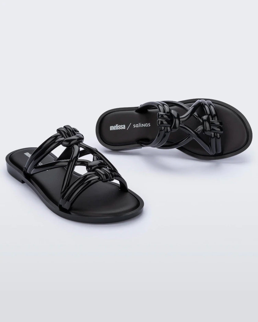 An angled front and top view of a pair of black Melissa Wave Slides with several front straps with knot like details.