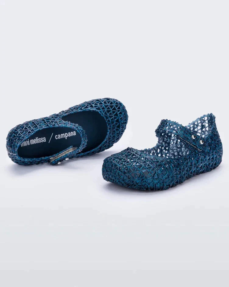 A side and top view of a pair of blue glitter Mini Melissa Campana flats with a snap strap for baby and an open woven texture.