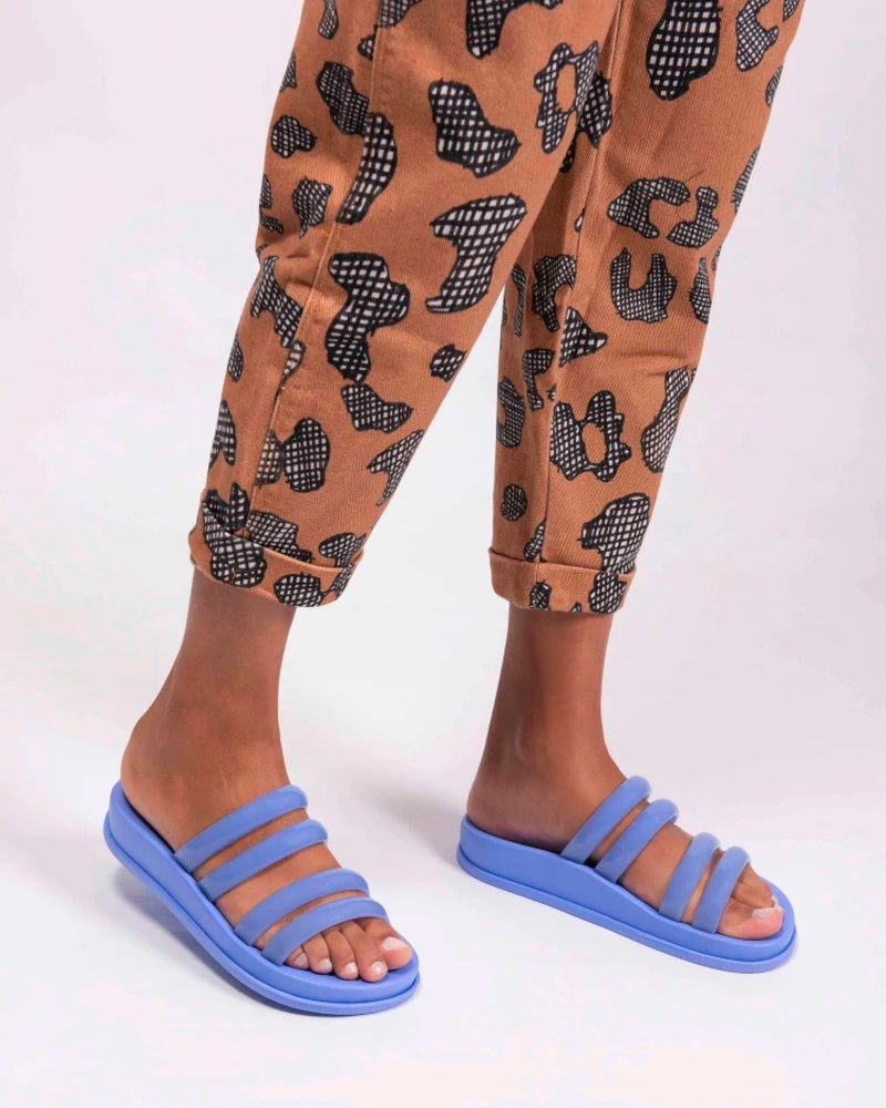 A model's legs wearing a pair of orange patterned pants and a pair of Blue Melissa Soft Wave Slides with 4 front straps.