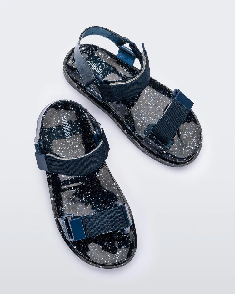 Top angled view of a pair of blue/silver glitter Melissa Wide Papete sandals with velcro ankle and front straps.