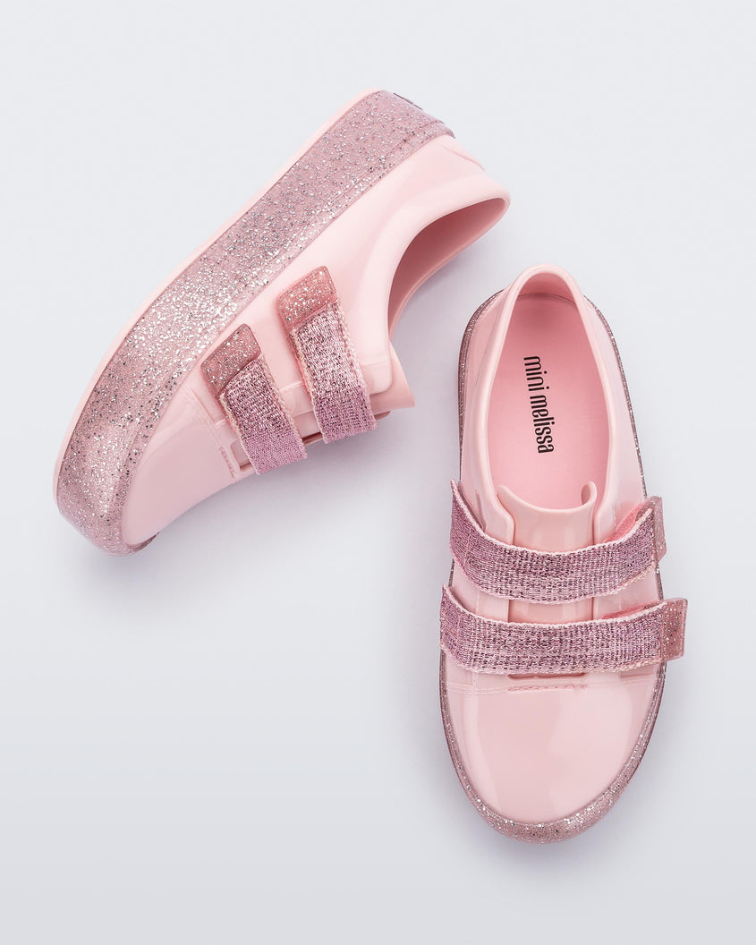 A top and side view of a pair of Pink/Pink Glitter Mini Melissa Beanny Bugs sneakers with a pink base, two shiny pink velcro straps and a pink glitter sole.