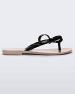 Side view of a beige/black Melissa Harmonic Sweet flip flop with a beige sole and black straps with a bow detail on the front.
