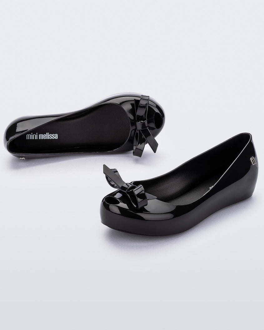 An angled front and top view of a Black Mini Melissa Ultragirl Bow flat with a black base and bow.