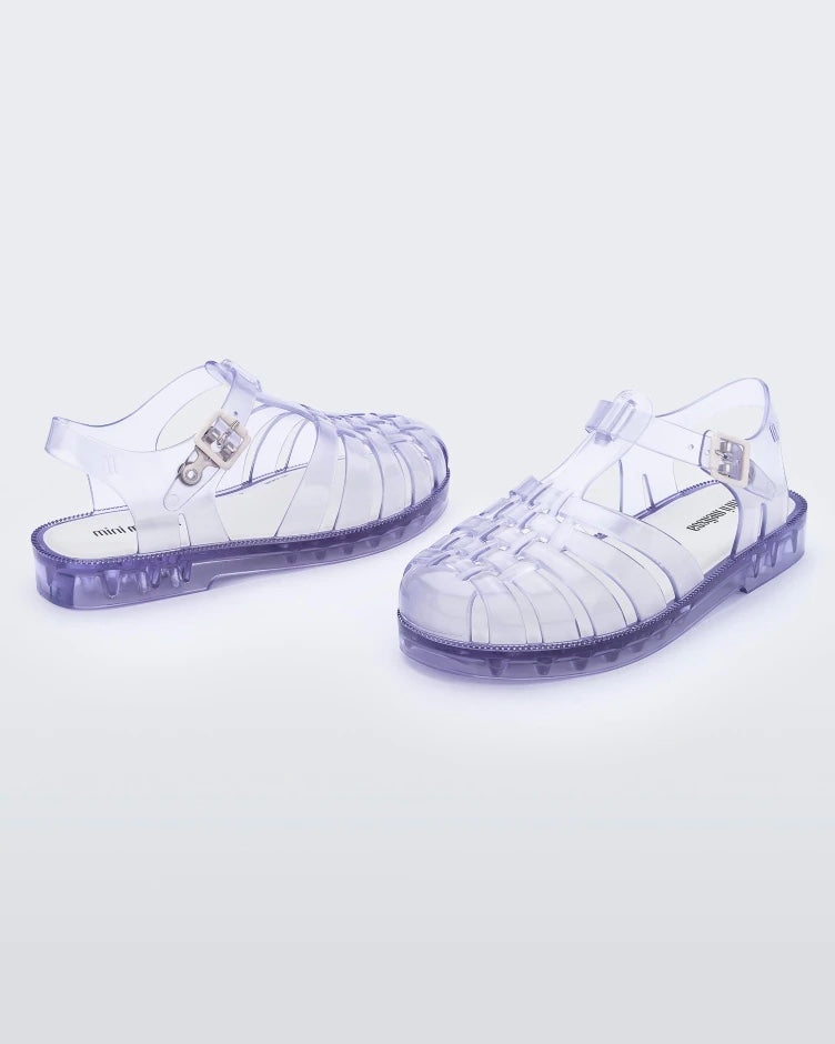 An angled front and side view of a pair of clear Mini Melissa Possession sandals with several straps and a clear base.