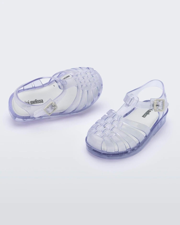 An angled front and top view of a pair of clear Mini Melissa Possession sandals with several straps and a closed toe front.