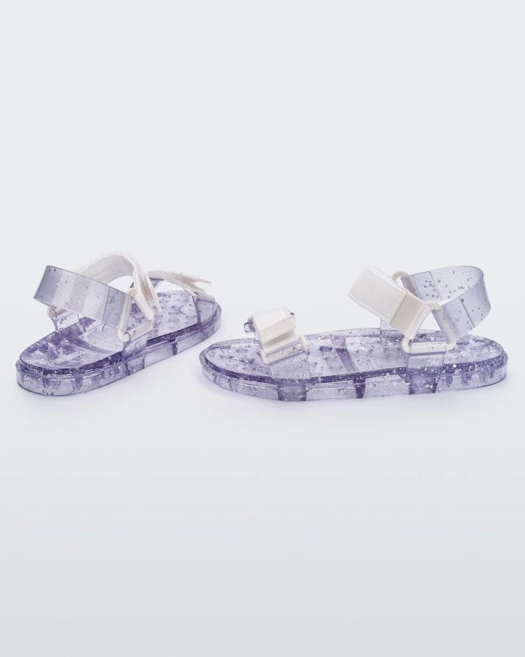 Angled view of a pair of Melissa Wide Papete sandals with transparent silver glitter sole with white/clear velcro straps 