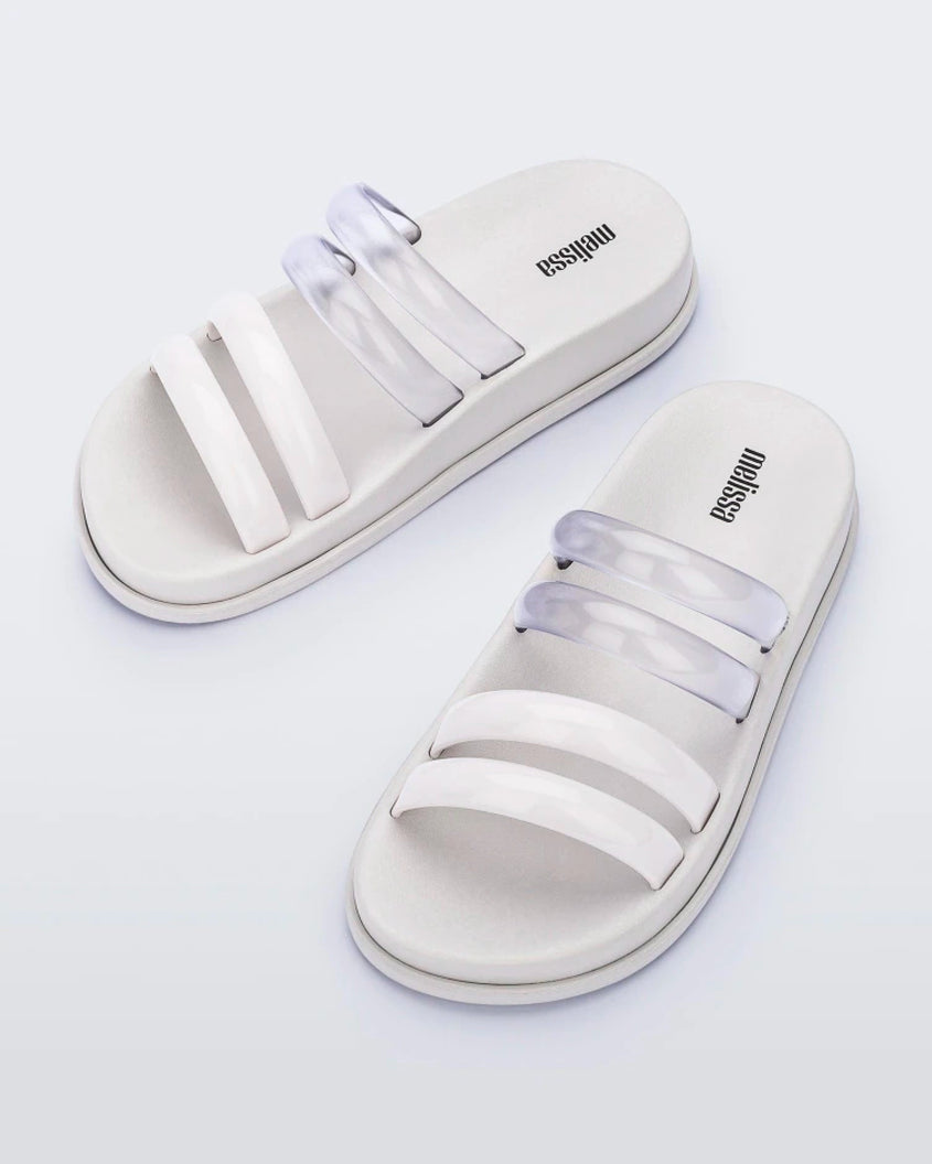 An angled top view of a pair of white/clear Melissa Soft Wave Slides with 4 straps: two clear and two white.