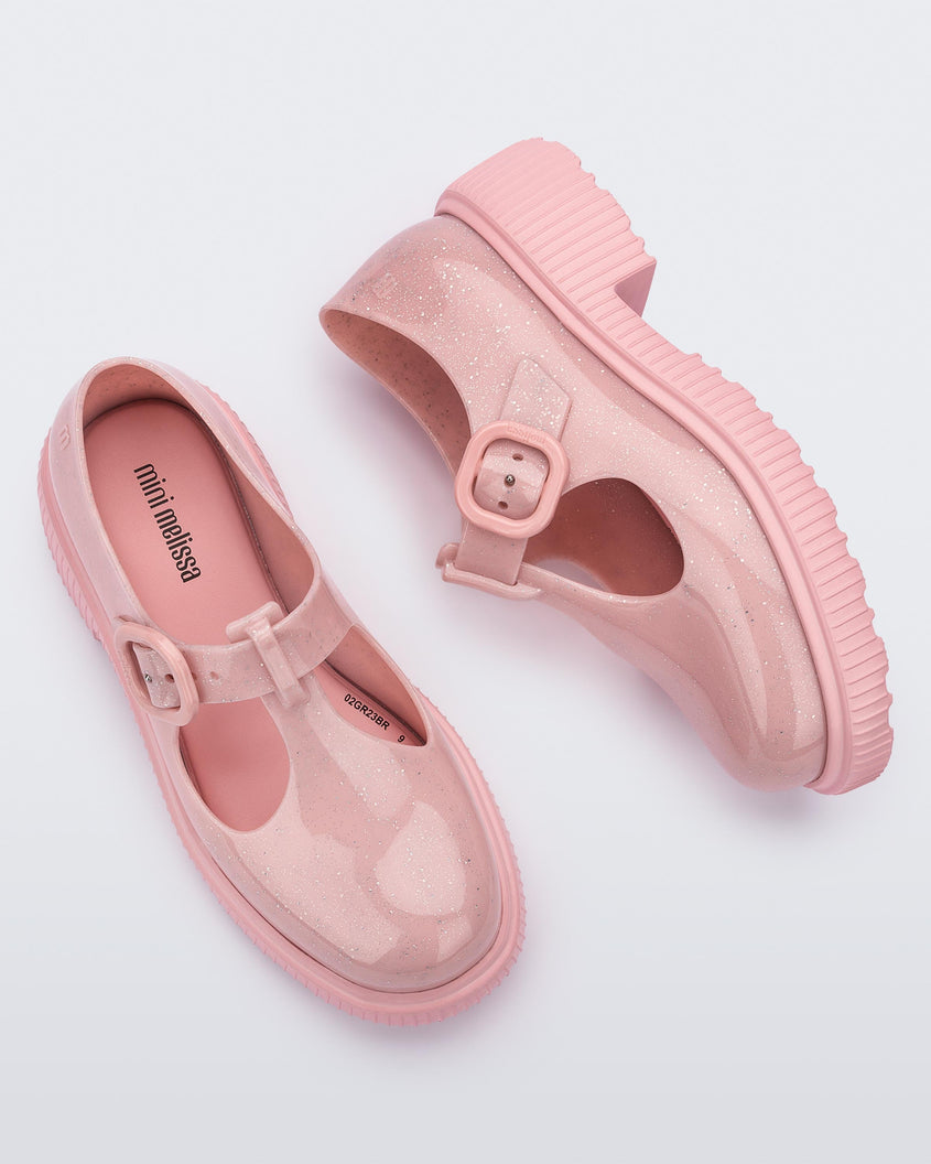 Top and side view of a pair of Pink Mini Melissa Jackie loafers with a pink glitter base, two cut outs, a pink buckle detail strap and pink sole.