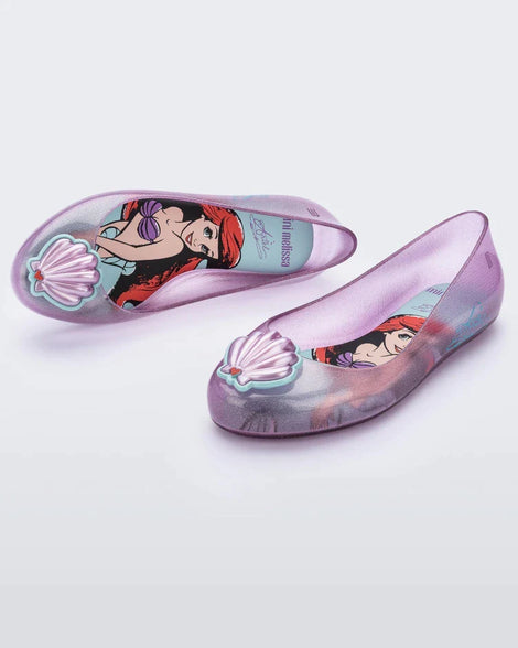 An angled front and top view of a pair of purple Mini Melissa Sweet Love Princess flats, with a purple base, Ariel in script on the side, a sea shell detail on the toe, and a drawing of Ariel of The Little Mermaid on the sole.