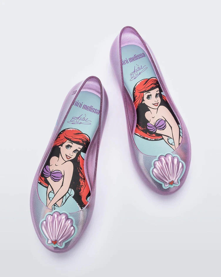 Top view of a pair of purple Mini Melissa Sweet Love Princess flats, with a purple base, Ariel in script on the side, a sea shell detail on the toe, and a drawing of Ariel of The Little Mermaid on the sole.