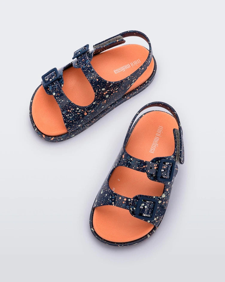 Top view of a pair of blue/orange Mini Melissa Wide Sandals with a blue base with a splatter painted print, and an orange insole.