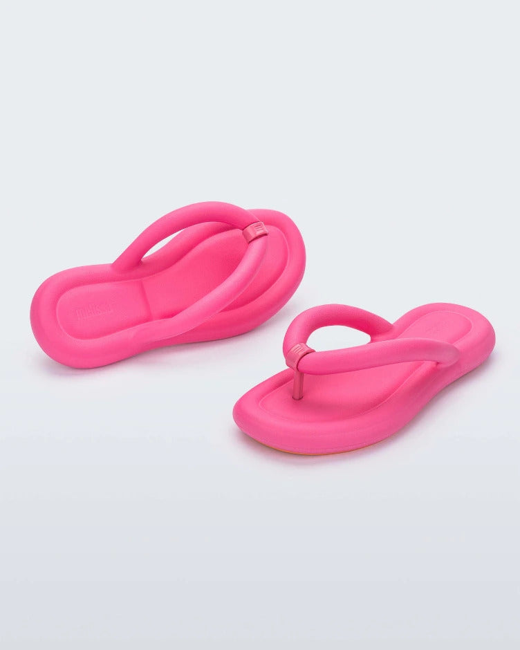 An angled back and front view of a pair of pink Melissa Free Flip Flops with puffer-like straps.