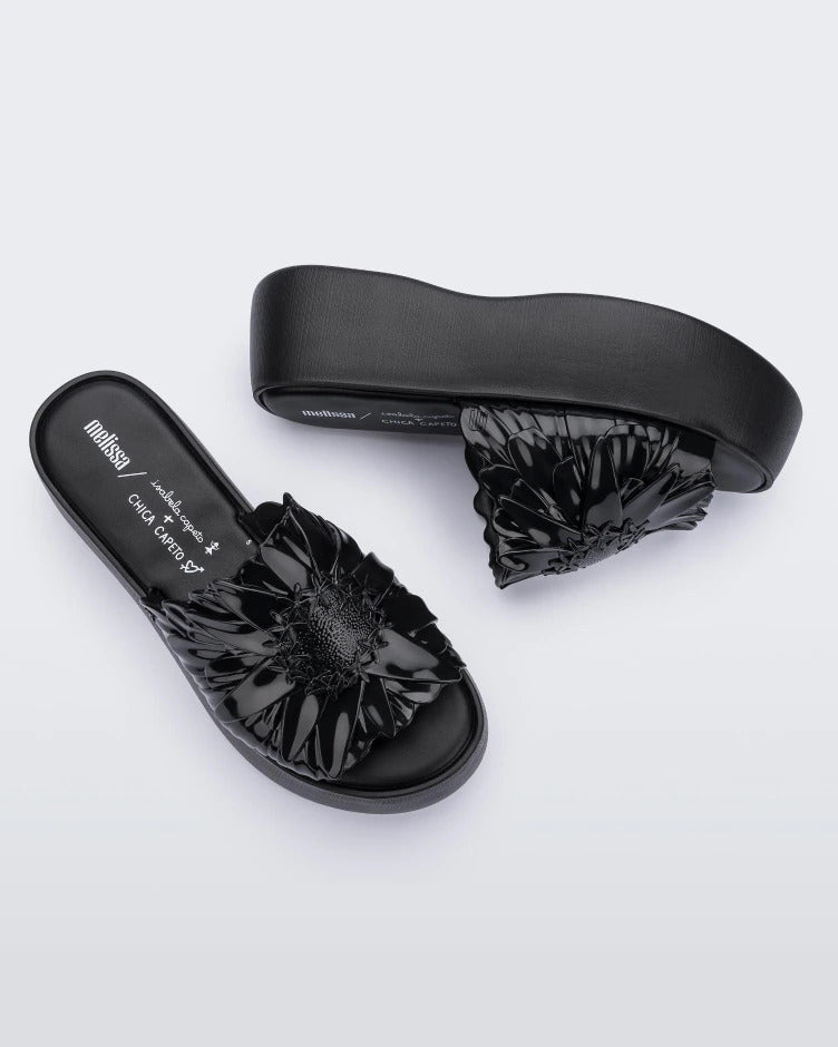 Top and side view of a pair of black Panc Becky platform slides with a flower design.