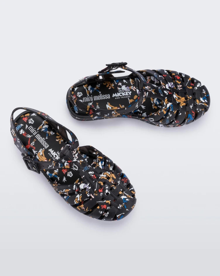 Top view of a pair of Mini Melissa Possession fisherman sandals in black with all over Disney character print. There is a buckle closure on the side of the ankle strap. 