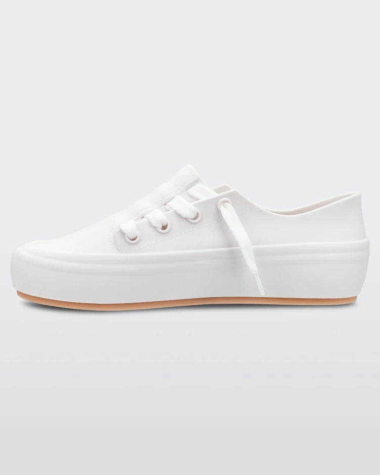 An inner side view of a white/beige Melissa Ulitsa sneaker with a white base, laces and a beige sole.