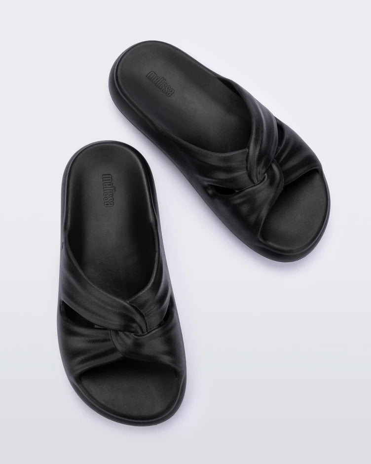 Top view of a pair of black Melissa Free Slides with a twist front detail.