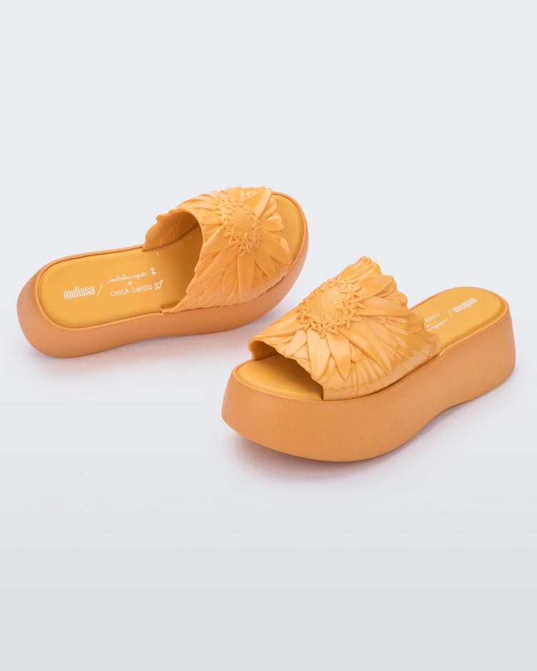 Angled view of a pair of yellow Melissa Panc Becky platform slides with a flower on the top.