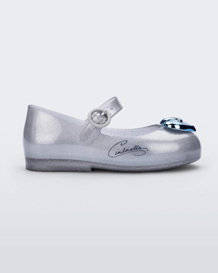 Side view of a silver Mini Melissa Sweet Love Princess flat with a top strap, silver base with Cinderella in script on the side, a blue heart detail on the toe and a drawing of Cinderella on the insole.