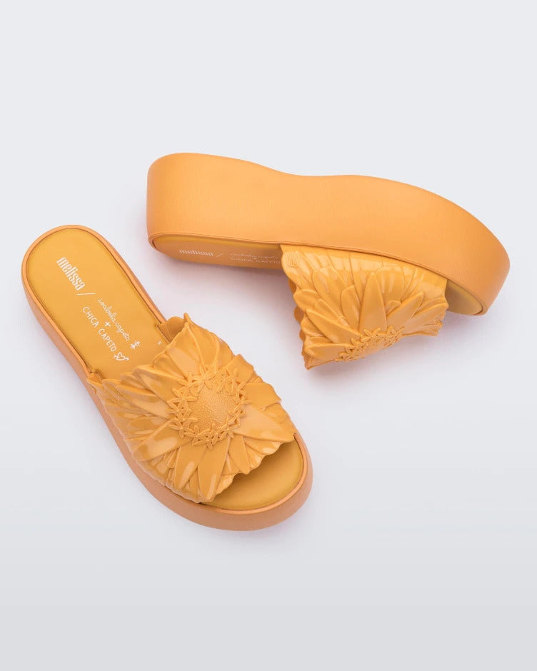 Angled view of a pair of yellow Melissa Panc Becky platform slides with a flower.