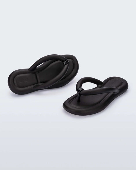 An angled back and front view of a pair of black Melissa Free Flip Flops with puffer-like straps.