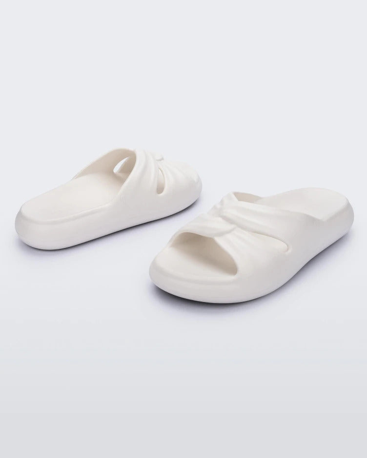An angled front and side view of a pair of white Melissa Free Slides with a twist front detail.