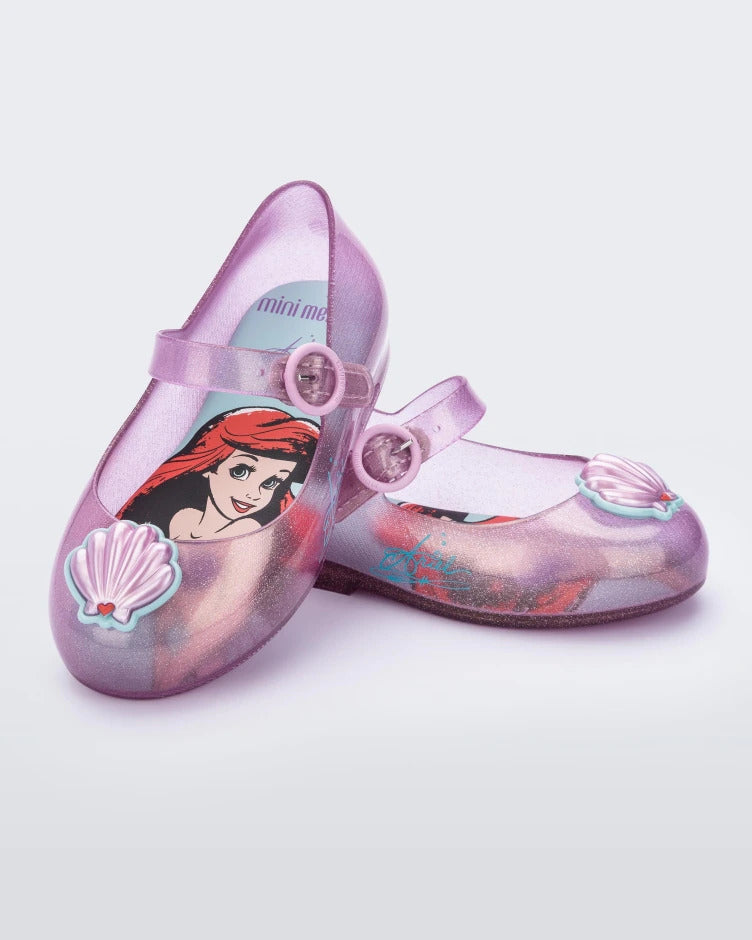 Angled top and side view of a pair of pink Mini Melissa Sweet Love Princess flats, with a pink base, a top strap, Ariel in script on the side, a shell detail on the toe, and a drawing of Ariel of The Little Mermaid on the insole.