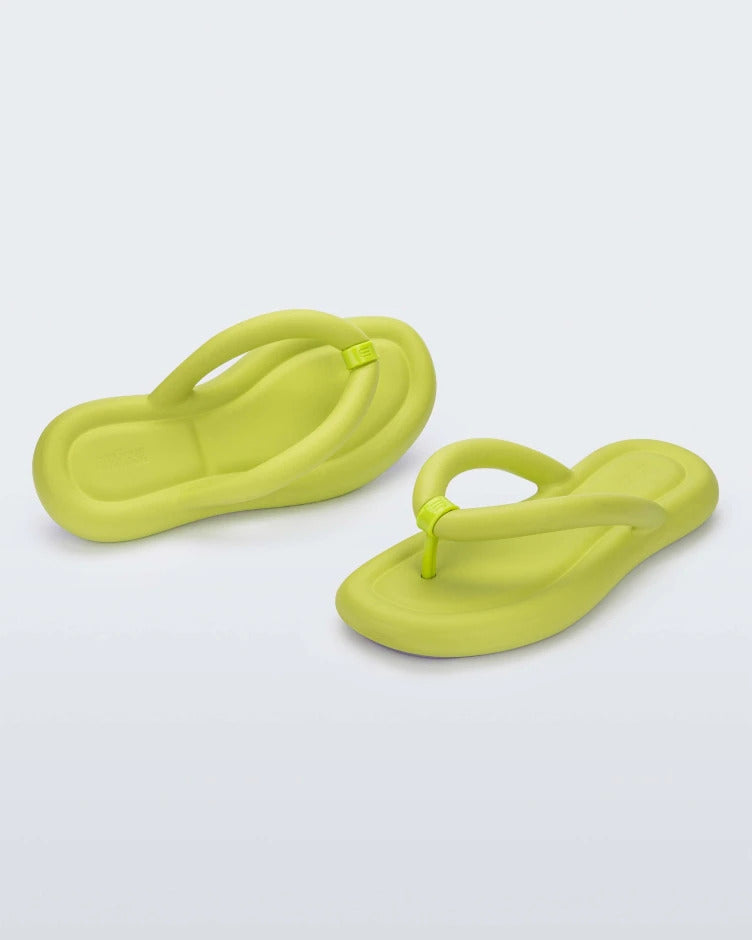 An angled front and side view of a pair of lime green Melissa Free Flip Flops with puffer-like straps.