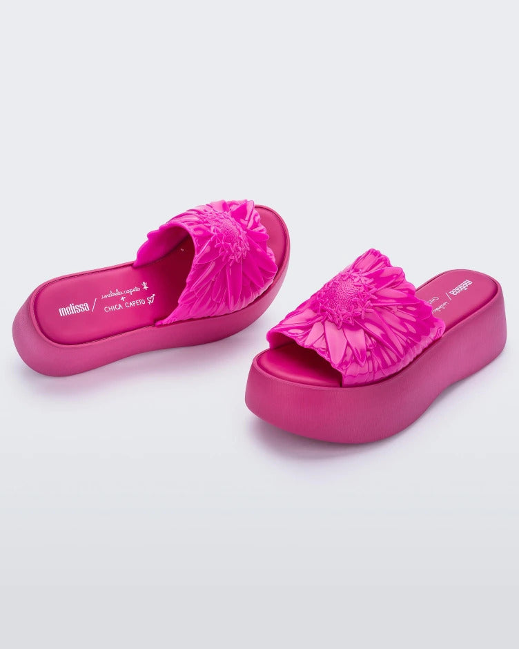 Angled view of a pair of pink Melissa Panc Becky platform slides with a flower on top.