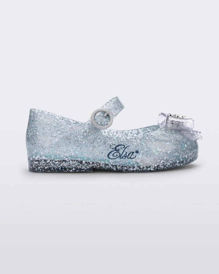 Side view of a glitter blue/blue Mini Melissa Sweet Love Princess flat, with a blue glitter base, a top strap, Elsa in script on the side, a bow detail on the toe, and a drawing of Elsa of Frozen on the sole.