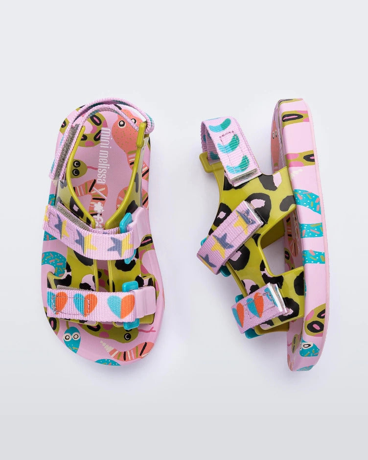 A top and side view of a pair of lilac/blue Mini Melissa Ping Pong sandals with a pink, green, black and blue patterned base and pink patterned velcro straps.