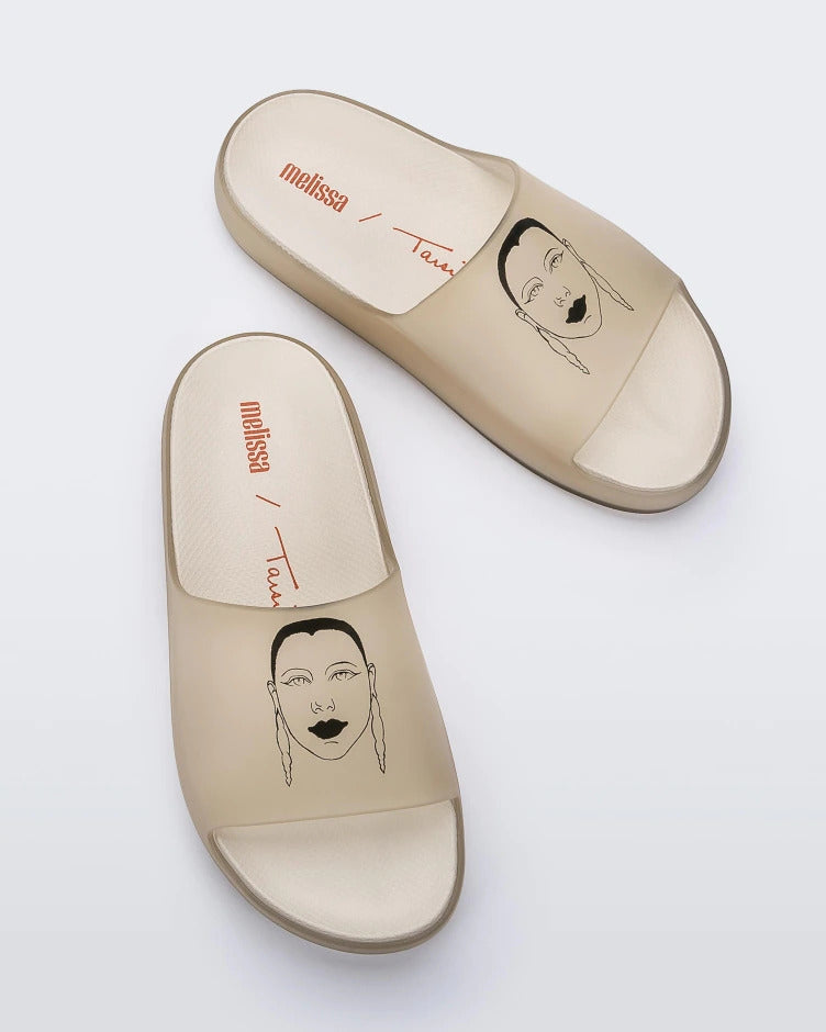 Top view of a pair of transparent beige Melissa Cloud slides with a drawing of a woman's face on the front.