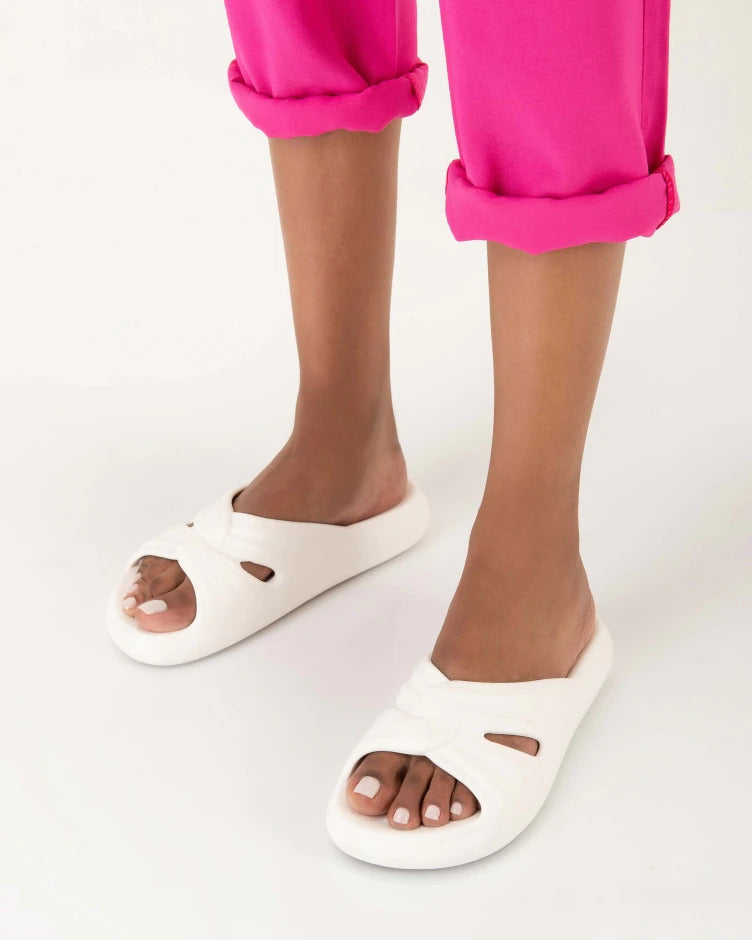 A model's legs wearing pink pants and a pair of white Melissa Free Slides with a twist front detail.