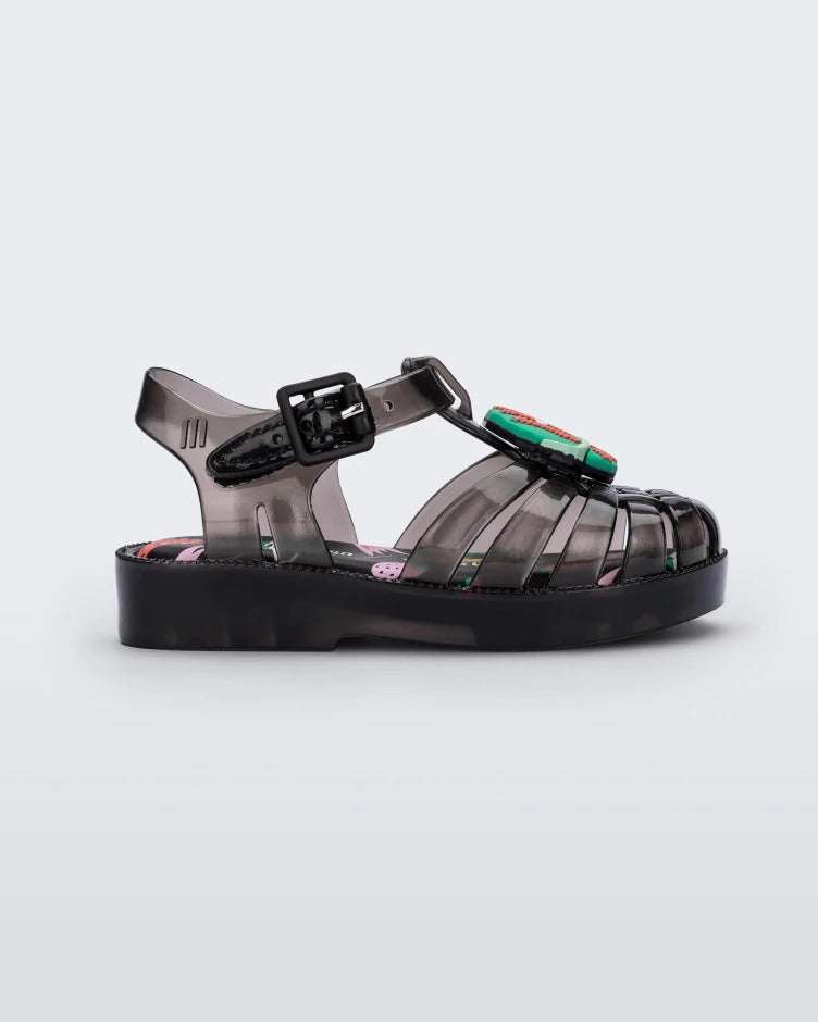 Side view of a Black Mini Melissa Possession sandal with several straps, a black base, and a cartoon drawing of a teal planet with a face on it.