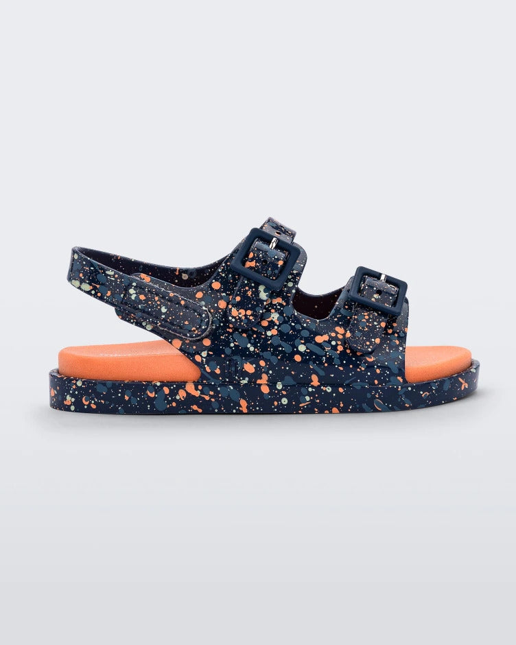 Side view of a blue/orange Mini Melissa Wide Sandal with a blue base with a splatter painted print, and an orange insole.