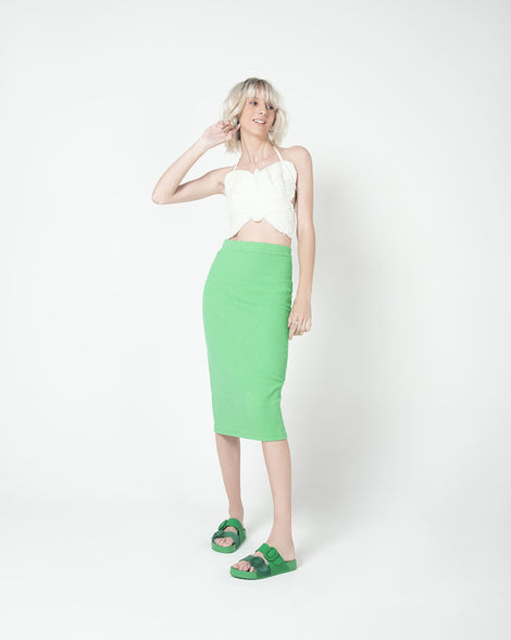 A model posing for a picture in a green skit, white top and a pair of Green Melissa Cozy slides with two green and transparent green straps with a buckle detail.