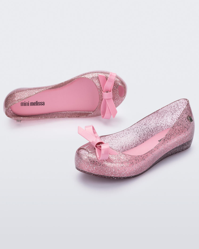 An angled top and side view of a Glitter Pink Mini Melissa Ultragirl Bow Glitter flat with a pink glitter base and pink bow