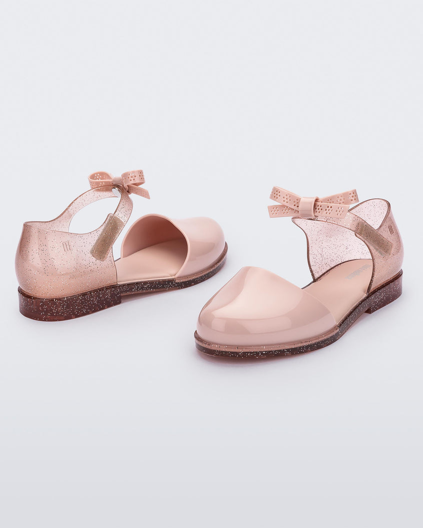 An angled front and back view of a pair of Mini Melissa Amy sandals with a pink closed toe section and a back pink glitter strap with a lace like bow detail.