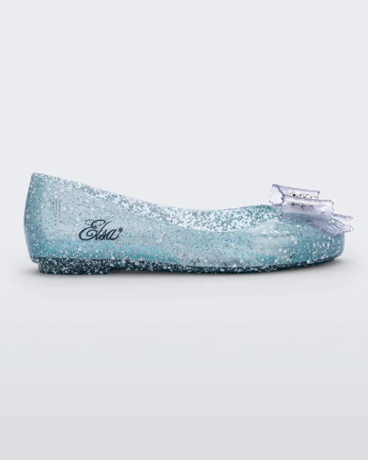 Side view of a clear Mini Melissa Sweet Love Princess flat, with a clear glitter base, Elsa in script on the side, a bow detail on the toe, and a drawing of Elsa of Frozen on the sole.