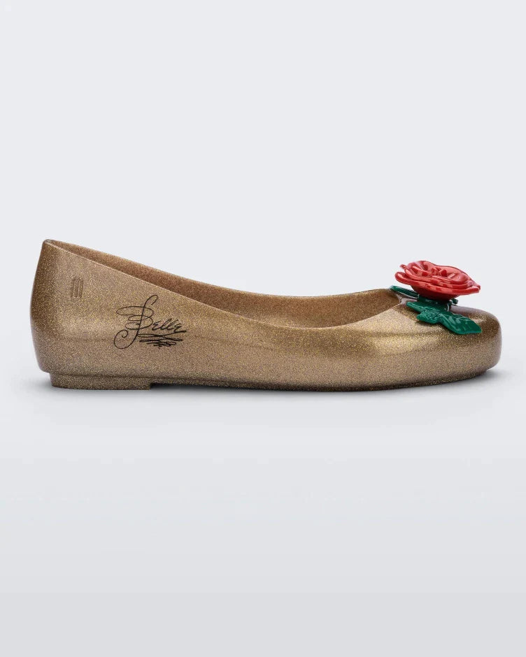Side view of a gold Mini Melissa Sweet Love Princess flat, with a gold base, Belle in script on the side, a rose detail on the toe, and a drawing of Belle of Beauty and the Beast on the sole.