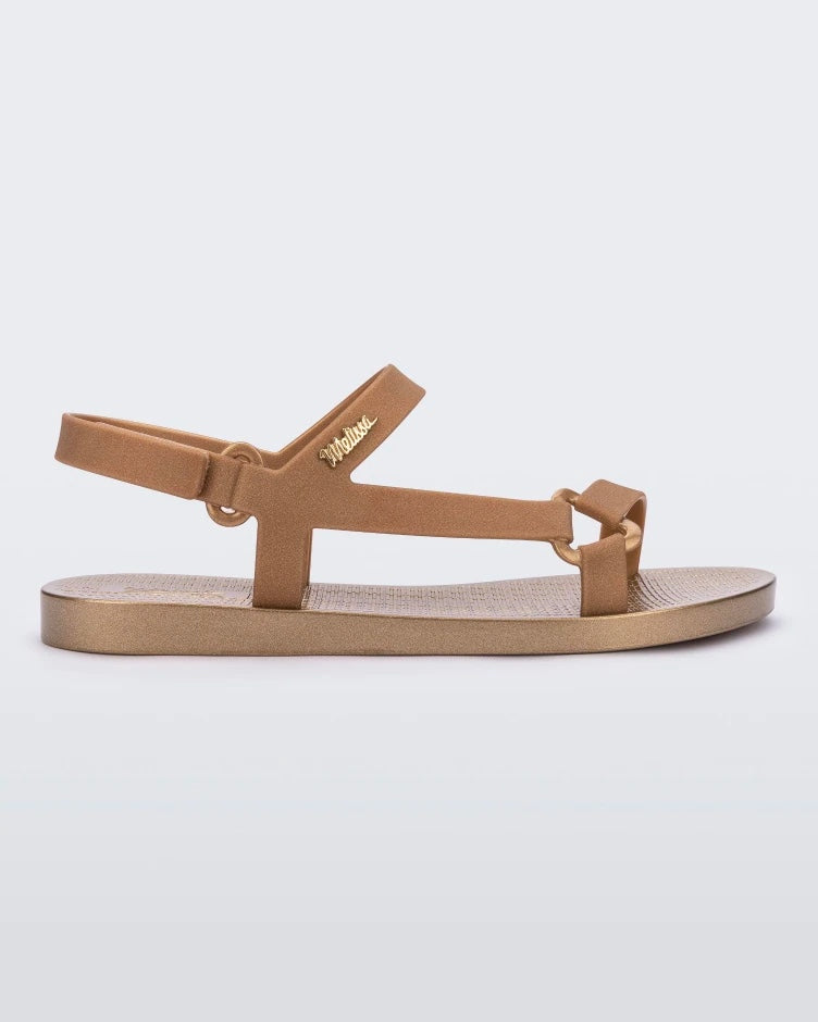 A side view of a gold metallic Melissa Sun Downtown sandal with a front and ankle strap joined together by a vertical strap and a triangle buckle.