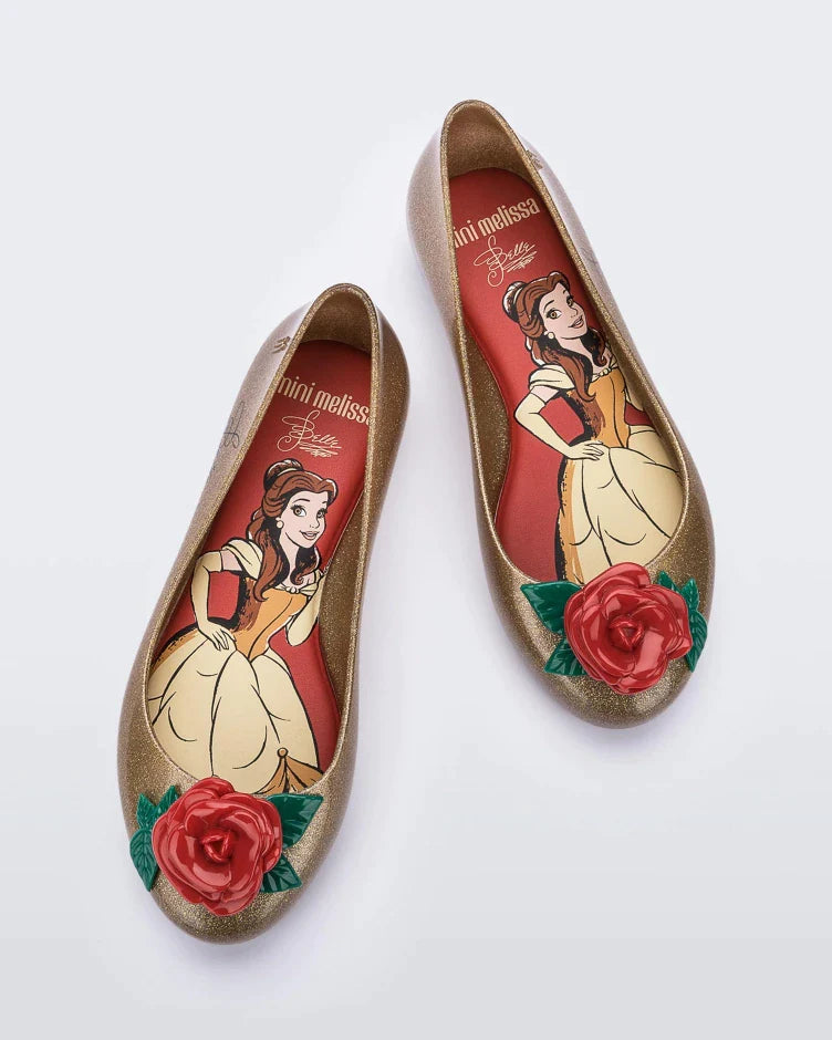 Top view of a pair of gold Mini Melissa Sweet Love Princess flats, with a gold base, Belle in script on the side, a rose detail on the toe, and a drawing of Belle of Beauty and the Beast on the sole.