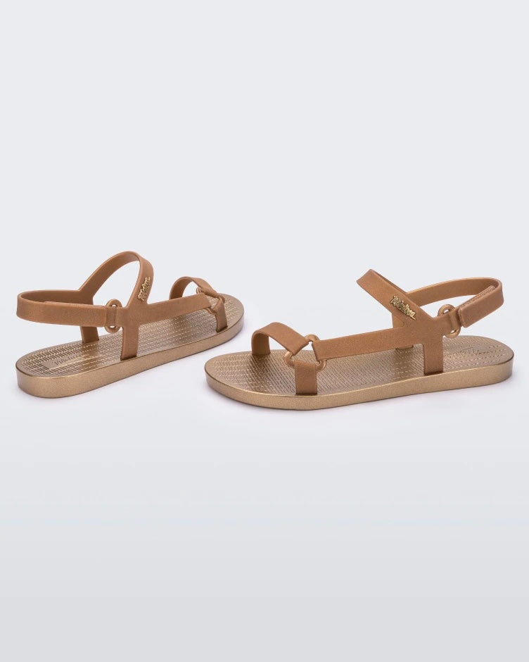 Side view of a pair of gold metallic Melissa Sun Downtown sandals with a front and ankle strap joined together by a vertical strap and a triangle buckle.