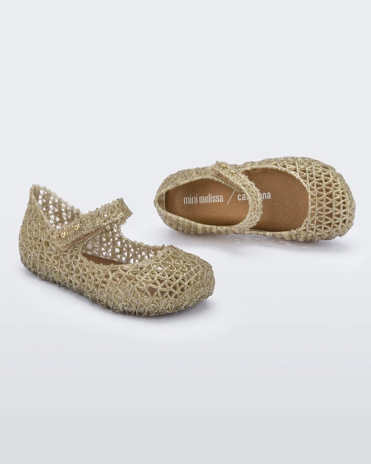 Top and side view of a pair of Mini Melissa Campana flats in gold for baby with an open woven texture. 