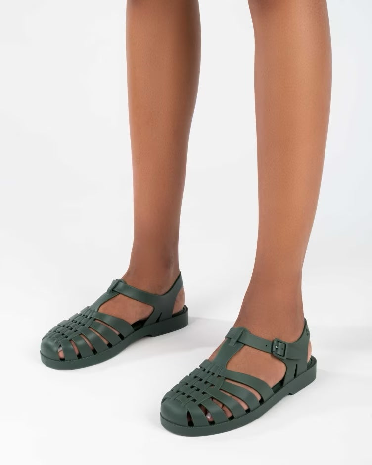 A model's legs wearing a pair of dark green Melissa Possession sandals with several straps and a closed toe front.