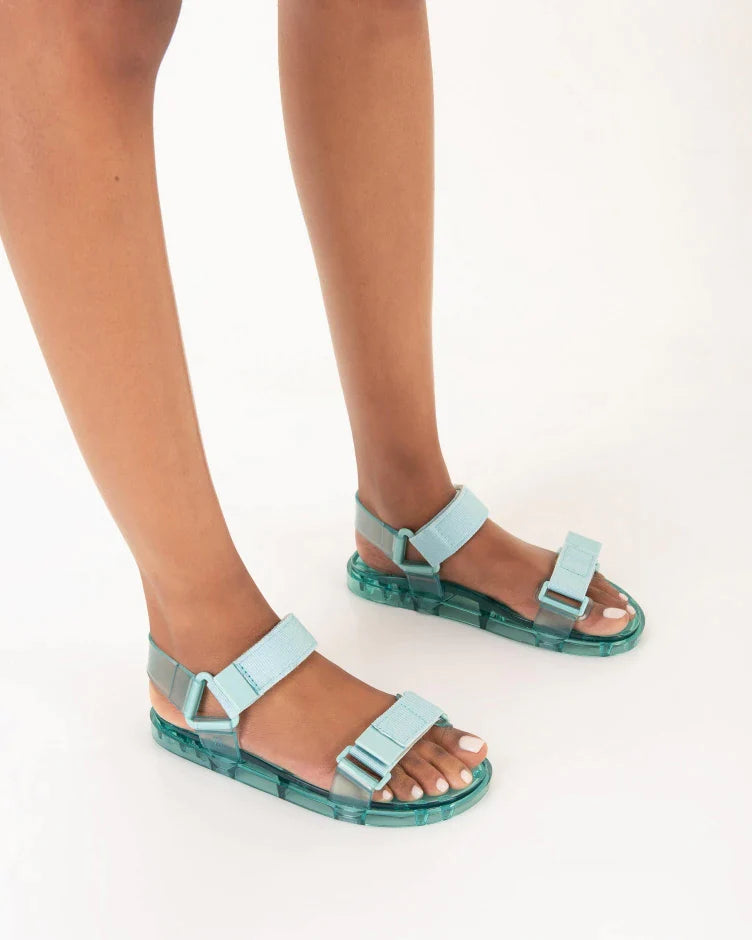 Model's legs wearing a pair of Melissa Wide Papete sandals with transparent green sole and green velcro straps