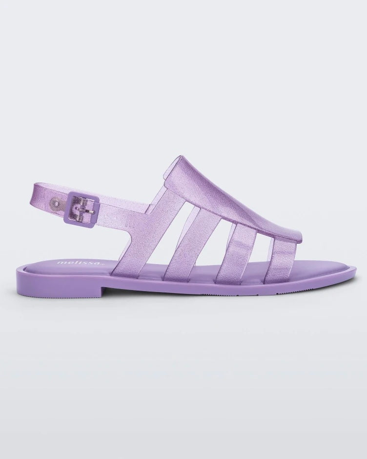 Side view of a transparent lilac glitter Melissa Boemia sandals with straps conjoining in the front and a back buckle.