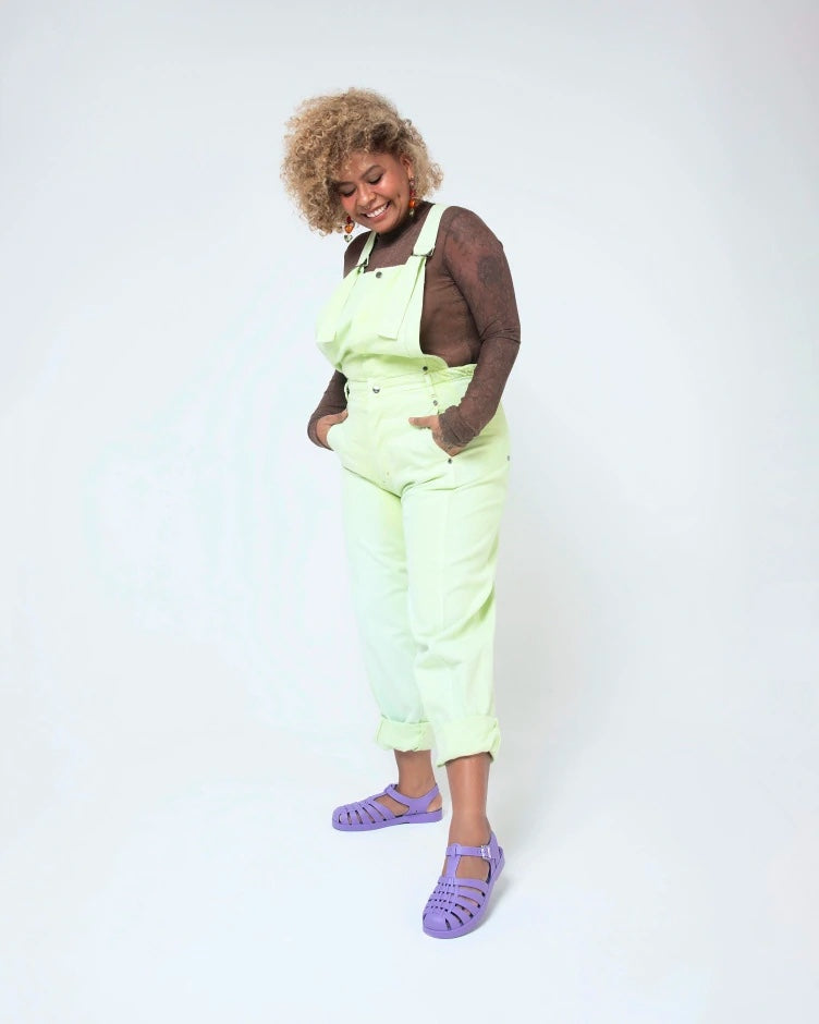 A model posing for a picture in a black top, green overalls and a pair of lilac Melissa Possession sandals with several straps and a closed toe front.