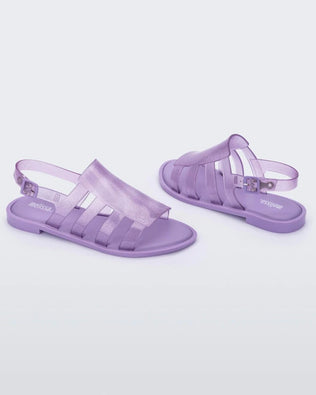 An angled inner and outter side view of a pair of transparent lilac glitter Melissa Boemia sandals with straps conjoining in the front and a back buckle.